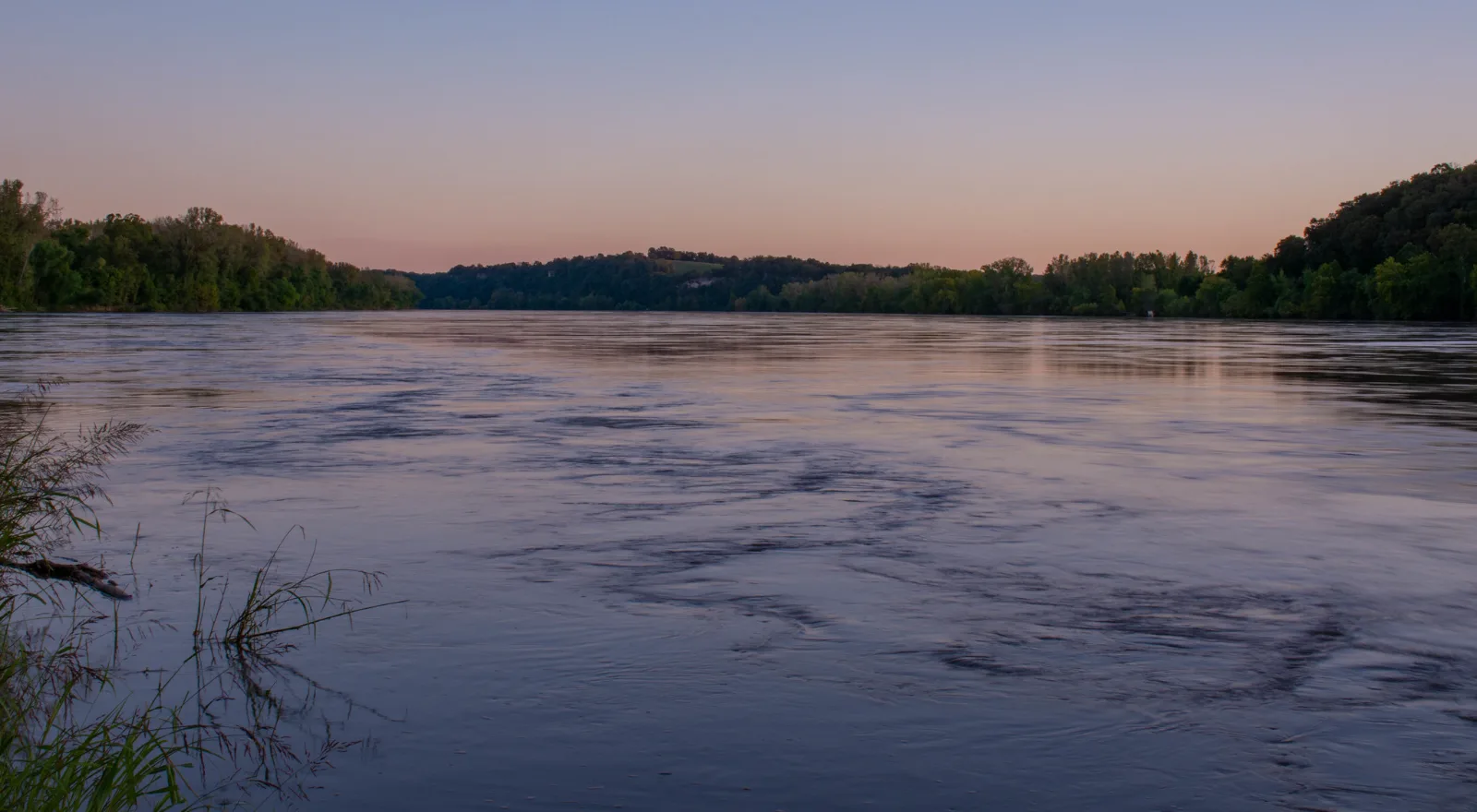 The Missouri River at dusk, bluffs and bottomland timber on the far bank