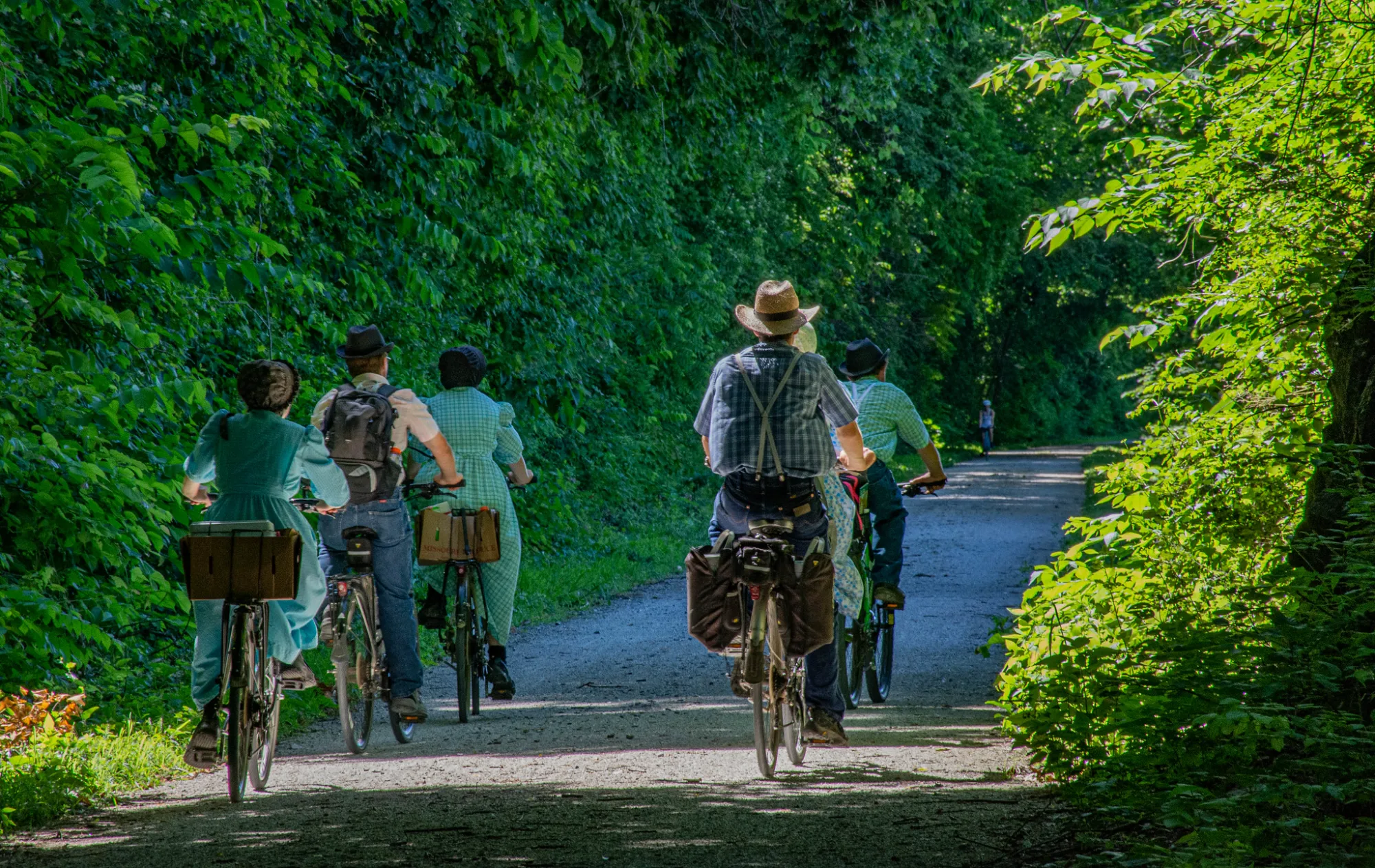 Riders on the crushed-limestone Katy Trail under a green summer canopy
